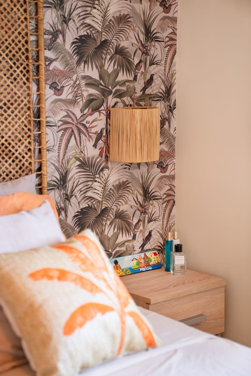 Detail van een slaapkamer met tropisch palmbehang, raffia wandlamp en houten nachtkastje