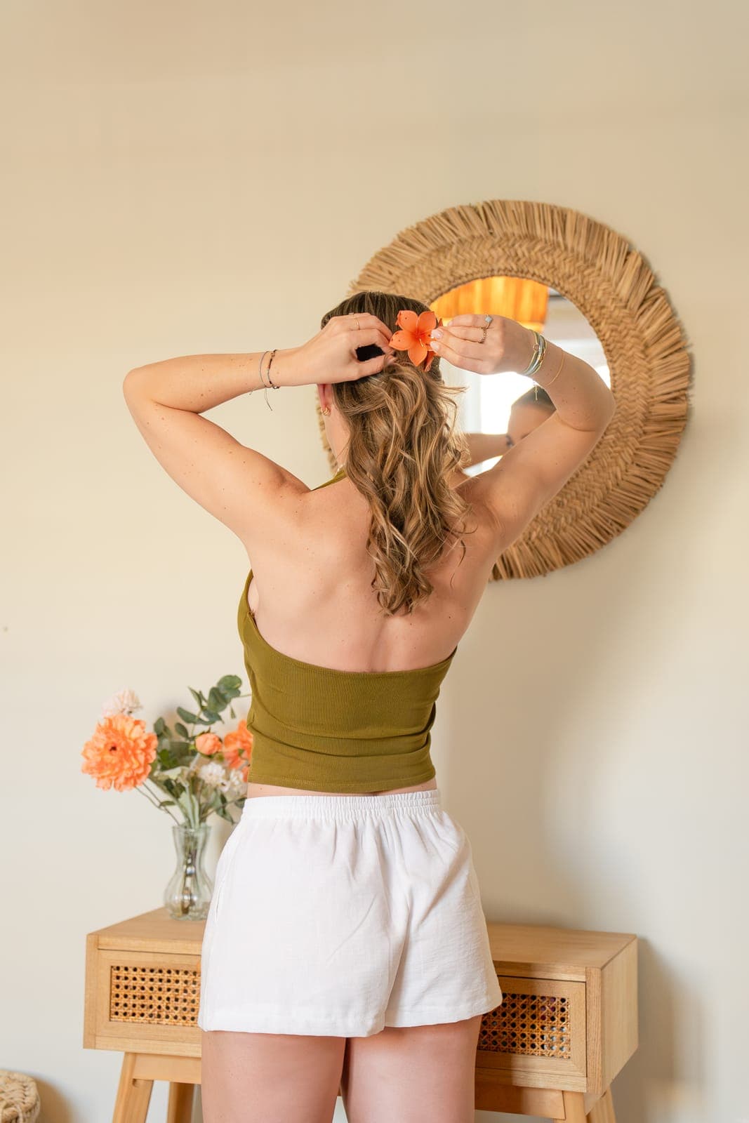 Vrouw steekt een oranje bloem in haar haar voor de raffia spiegel in de slaapkamer