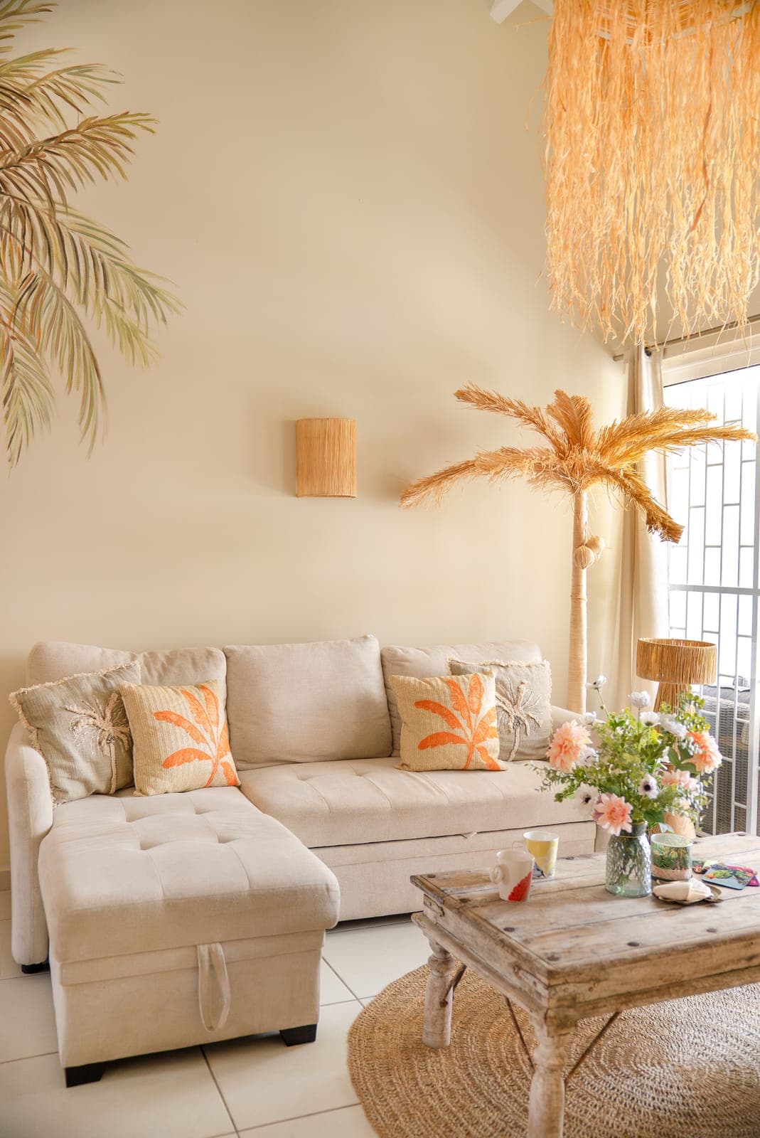 Woonkamer met beige hoekbank, palmkussens, raffia lamp en decoratieve palmboom